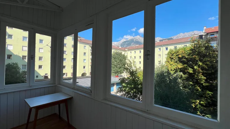 Heller Wintergarten mit Bergblick und Blick auf umliegende Gebäude, ideal zum Entspannen.
