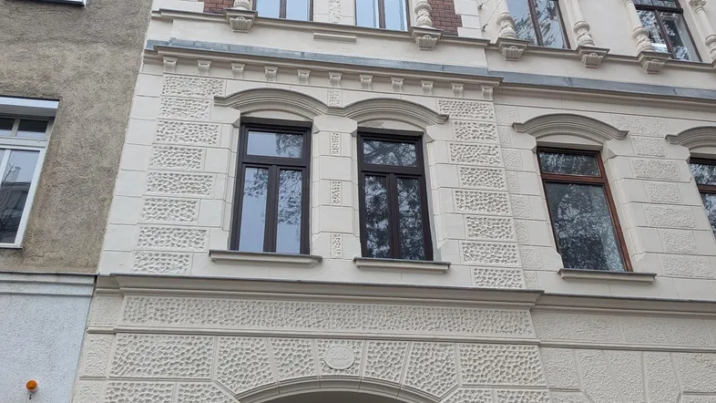 Historisches Mehrfamilienhaus mit aufwendiger Stuckfassade und großen Fenstern in der Stadt.
