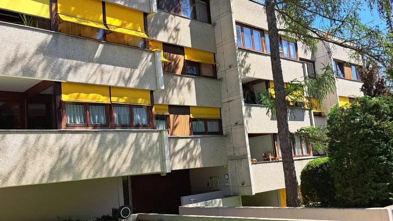 Modernes Mehrfamilienhaus mit gelben Markisen und gepflegter Grünfläche im Vordergrund.