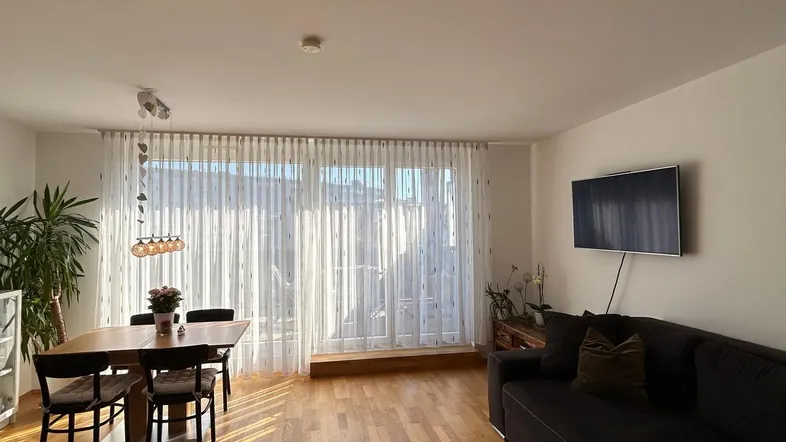 Helles Wohn- und Esszimmer mit Holzboden, großem Sofa und Zugang zum Balkon.