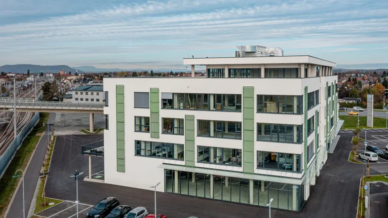 Moderne Bürogebäude-Architektur mit großen Fenstern und Parkplätzen unter einem bewölkten Himmel.