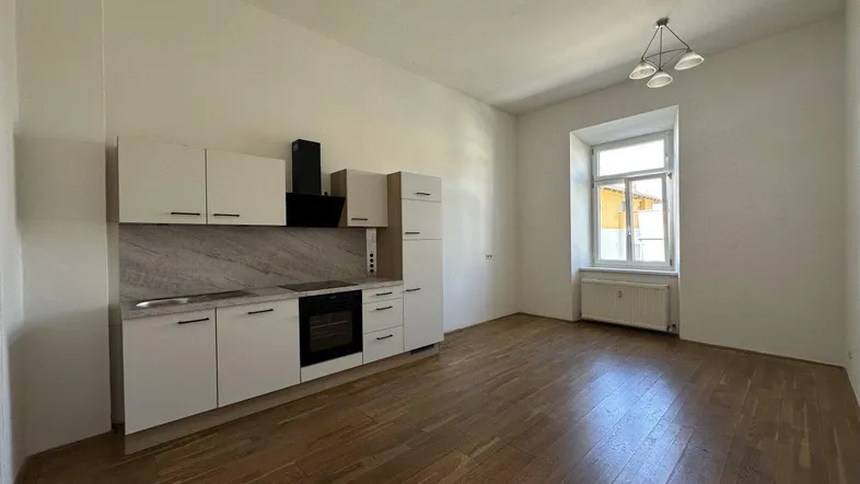 Helle Wohnküche mit neuer Einbauküche, Parkettboden und Fenster mit Tageslicht.