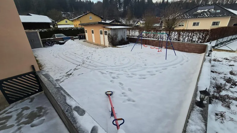Schneebedeckter Gartenbereich mit Spielgeräten und Blick auf die umliegende Landschaft.