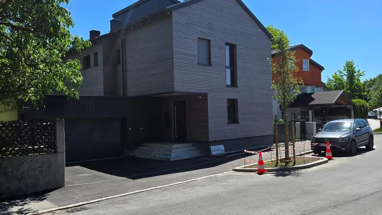 Modernes Zweifamilienhaus mit Holzfassade und integrierter Garage an einer ruhigen Straße gelegen.