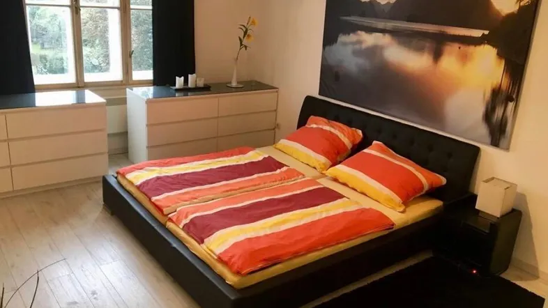 Helles Schlafzimmer mit Doppelbett, zwei Kommoden und einem großen Fenster mit Blick ins Grüne.