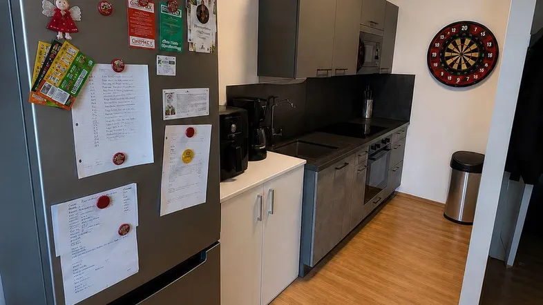 Kleine, funktionale Küche mit modernen grauen Schränken, integrierten Geräten und Holzboden.