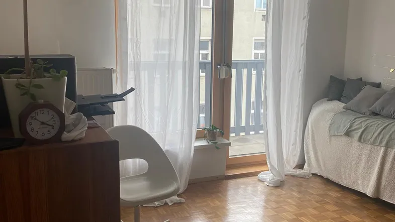 Helles Schlafzimmer mit Parkettboden, Schreibtisch und Zugang zum Balkon.