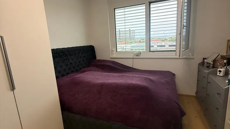 Helles Schlafzimmer mit Holzboden, großem Bett und Blick nach draußen durch das Fenster.