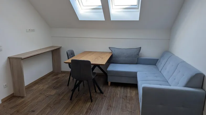 Helles Wohnzimmer im Dachgeschoss mit gemütlichem Sofa, Esstisch und Dachfenstern für viel Tageslicht.