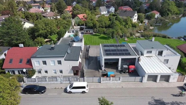 Luftaufnahme des Anwesens mit mehreren Gebäuden, Garagen und angrenzendem See.