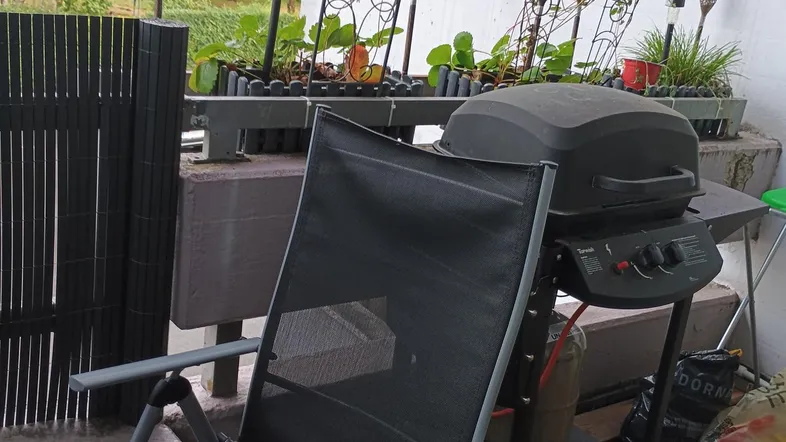 Gemütlicher Balkon mit Grillbereich, Pflanzen und einem entspannten Blick ins Grüne.
