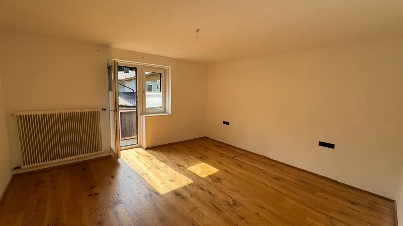 Helles Zimmer mit Holzboden und Zugang zu einem kleinen Balkon, ideal als Wohn- oder Schlafbereich.