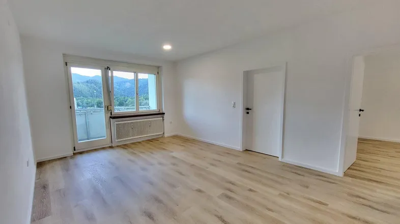 Helles Wohnzimmer mit neuem Laminatboden und Zugang zu einem Balkon mit Bergblick.