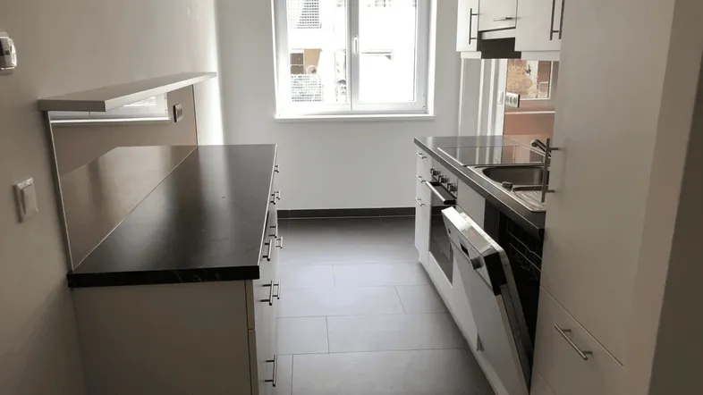 Helle Küche mit Einbaugeräten, dunkler Arbeitsplatte und Fensterblick auf den Innenhof.