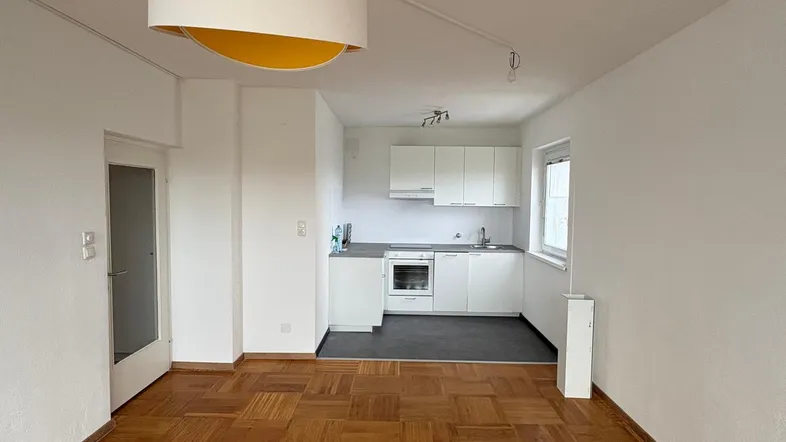 Heller Wohnbereich mit Parkettboden und integrierter Küchenzeile, ideal für offenes Wohnen.