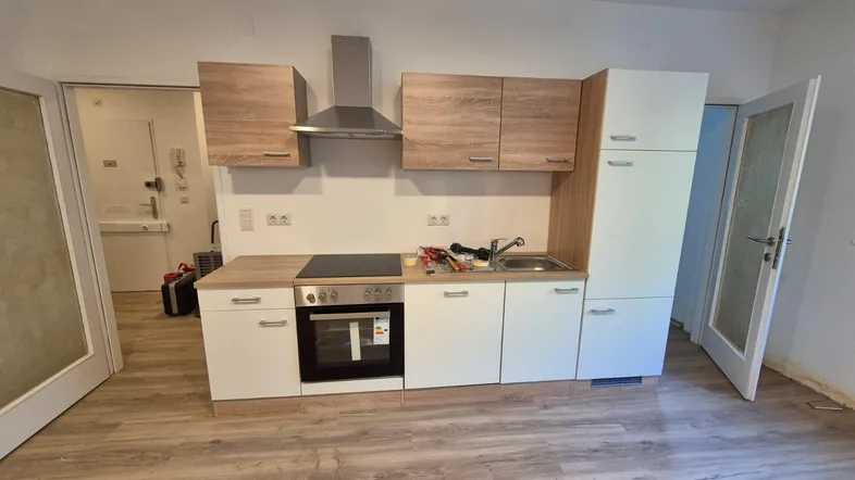 Neue Einbauküche mit hellen Holz- und weißen Fronten, ausgestattet mit Herd, Dunstabzugshaube und Laminatboden.
