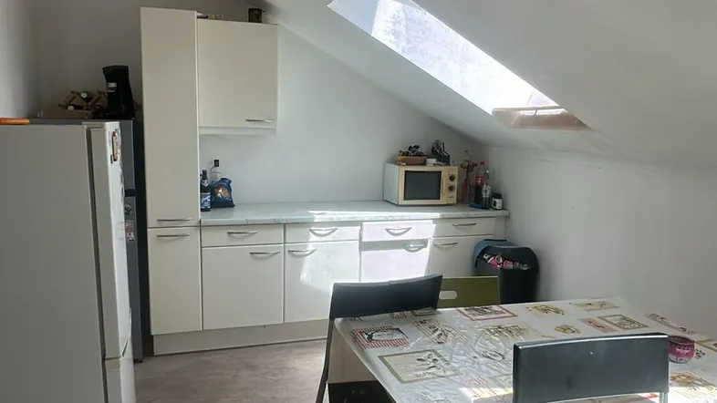 Helle Dachgeschossküche mit weißer Einbauküche, Esstisch und Dachfenster für natürliches Licht.