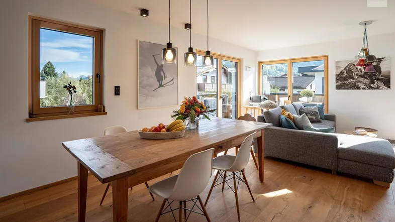 Helles Wohn-Esszimmer mit Holzboden, großem Esstisch und gemütlicher Sofaecke mit Bergblick.
