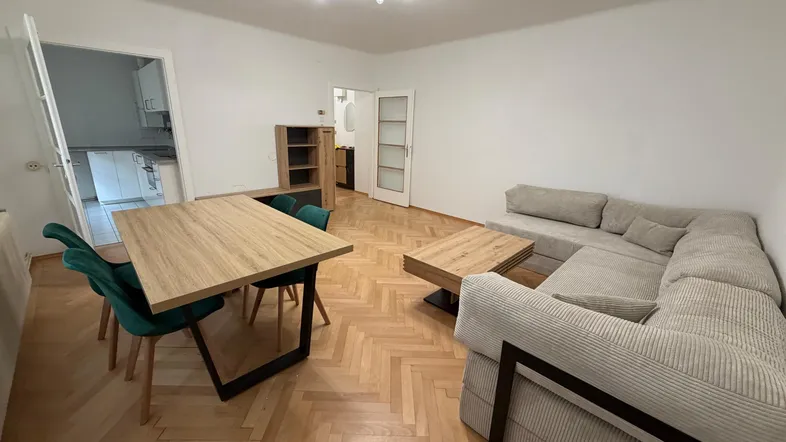 Geräumiger Wohn- und Essbereich mit beigem Ecksofa und Zugang zu Küche und Bad.