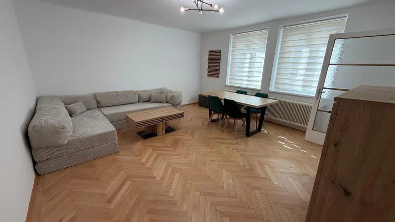 Heller Wohn- und Essbereich mit modernem Sofa, Esstisch und Fischgrätparkett.