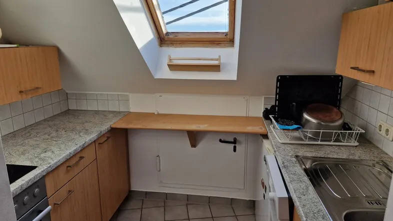 Dachschrägenküche mit Fliesenboden, Arbeitsplatte, Dachfenster und grundlegender Ausstattung.