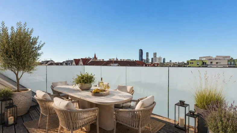 Elegante Dachterrasse mit Esstisch, Pflanzen und Blick auf die Stadt unter blauem Himmel.