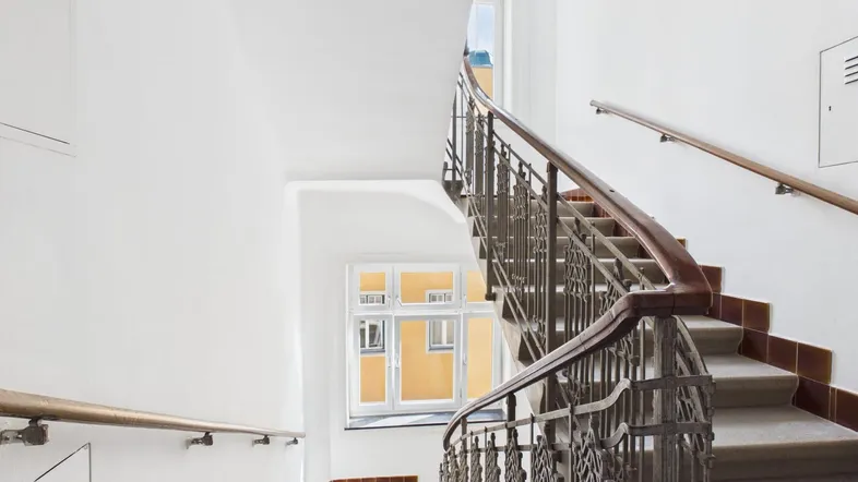 Helles Treppenhaus mit schmiedeeisernem Geländer und natürlichem Lichteinfall durch ein Fenster.