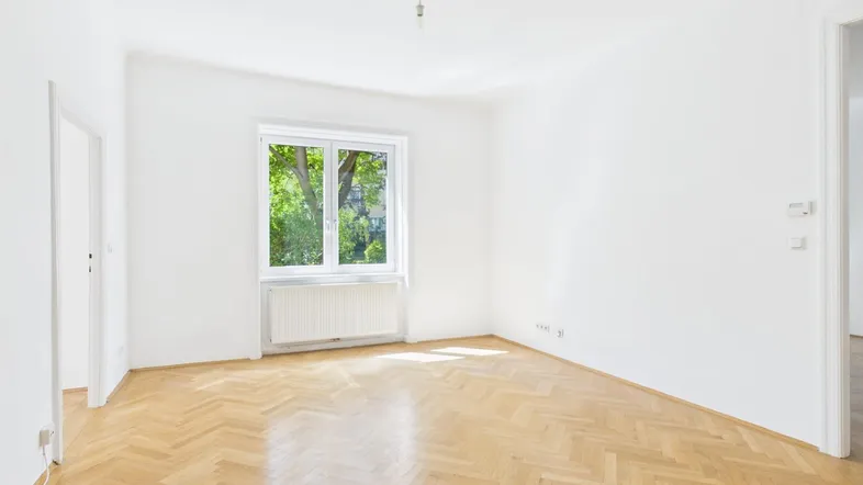 Helles Zimmer mit Fischgrätparkettboden, weißen Wänden und Blick ins Grüne.