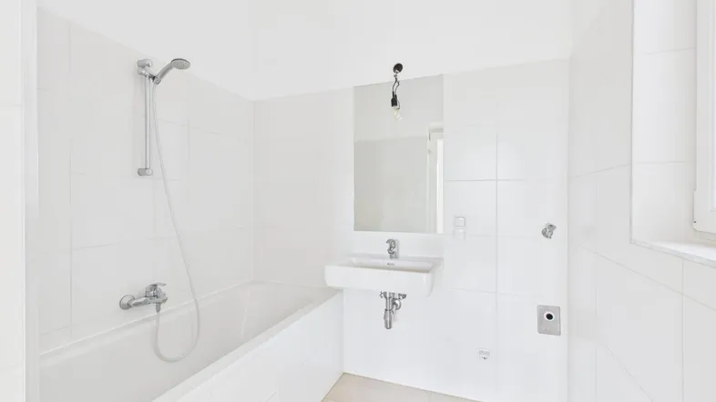 Helles Badezimmer mit weißen Fliesen, Badewanne mit Duschfunktion und einem Fenster für Tageslicht.