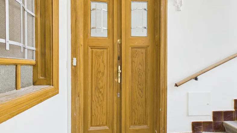 Holztür mit Glaseinsätzen im Treppenhaus eines Mehrfamilienhauses, umgeben von weißen Wänden.