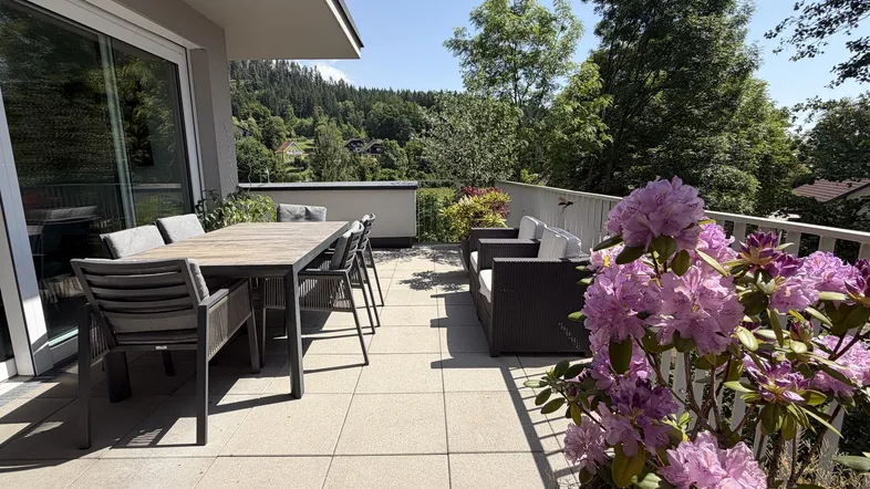 Geräumige Sonnenterrasse mit Esstisch und Lounge-Möbeln, umgeben von üppigem Grün und Bergblick.