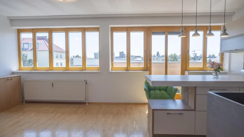 Heller Wohnbereich mit Holzboden, großen Fenstern und Blick auf die offene Küche.