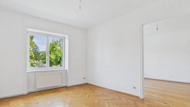 Helles Zimmer mit Fischgrätparkett und Blick ins Grüne, ideal als Wohn- oder Schlafzimmer.