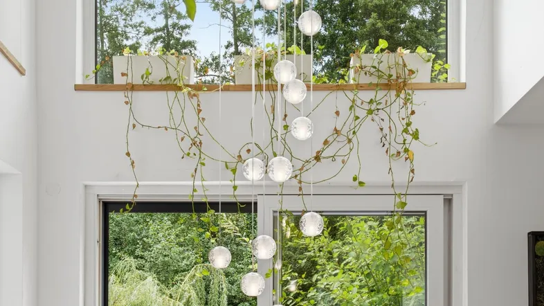 Hohe Decke mit moderner Hängeleuchte und Blick ins Grüne durch große Fenster.