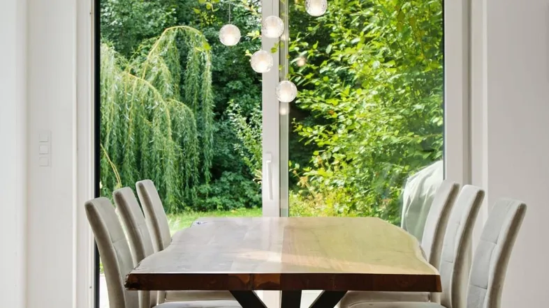 Heller Essbereich mit Holztisch, modernen Stühlen und Blick ins Grüne durch große Fenster.