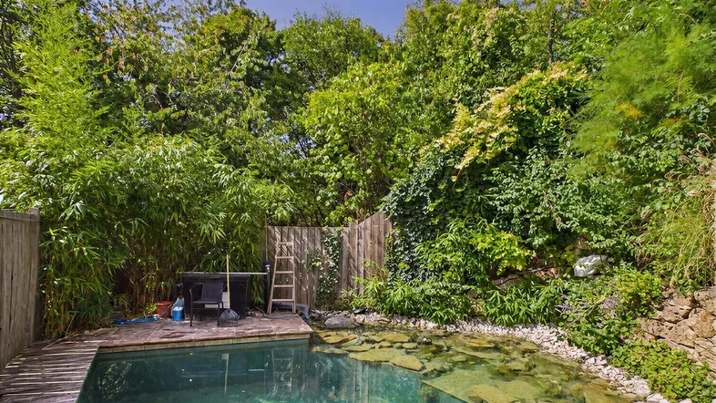 Natürlicher Poolbereich mit Holzdeck, umgeben von üppiger Vegetation und Steinmauern.