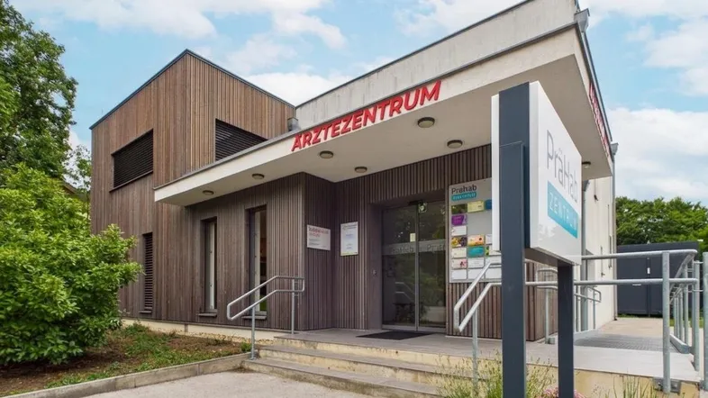 Modernes Ärztezentrum mit Holzfassade und klarem Eingangsbereich, umgeben von Grünflächen.