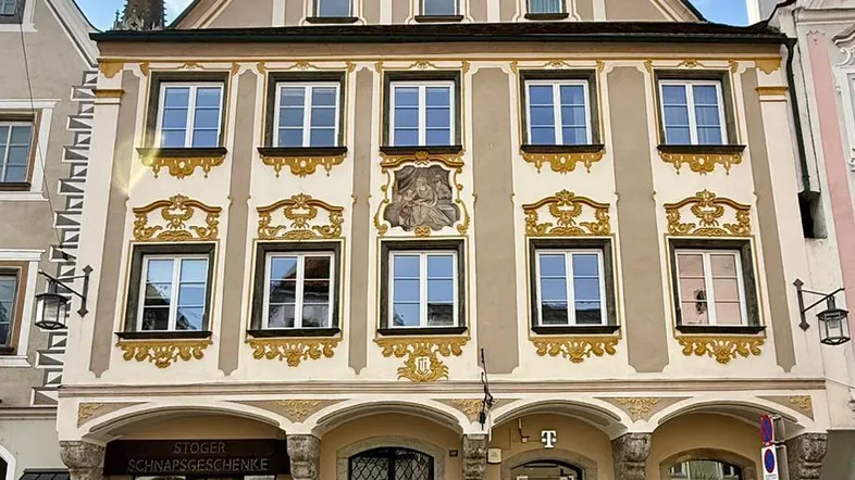Historisches Gebäude mit aufwendig verzierter Fassade und Geschäften im Erdgeschoss an einer Kopfsteinpflasterstraße.