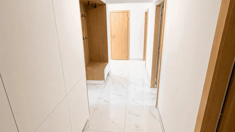 Heller Flur mit modernen weißen Fliesen in Marmoroptik und integrierter Garderobe.