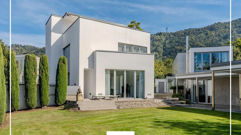Moderne weiße Villa mit weitläufigem Rasen und hohen Zypressen unter blauem Himmel.