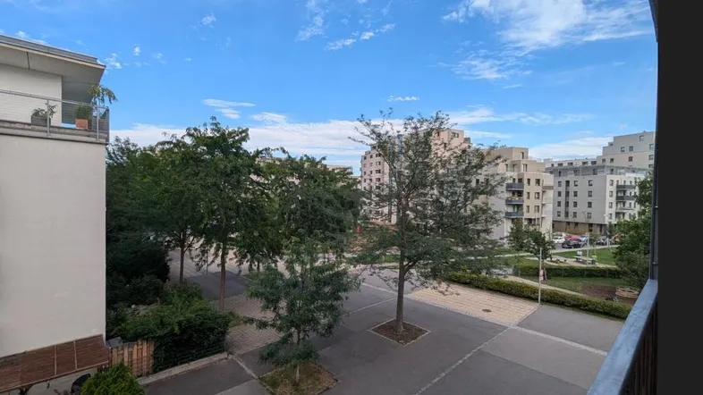 Blick von einem Balkon auf einen begrünten Innenhof mit Bäumen und modernen Wohngebäuden.