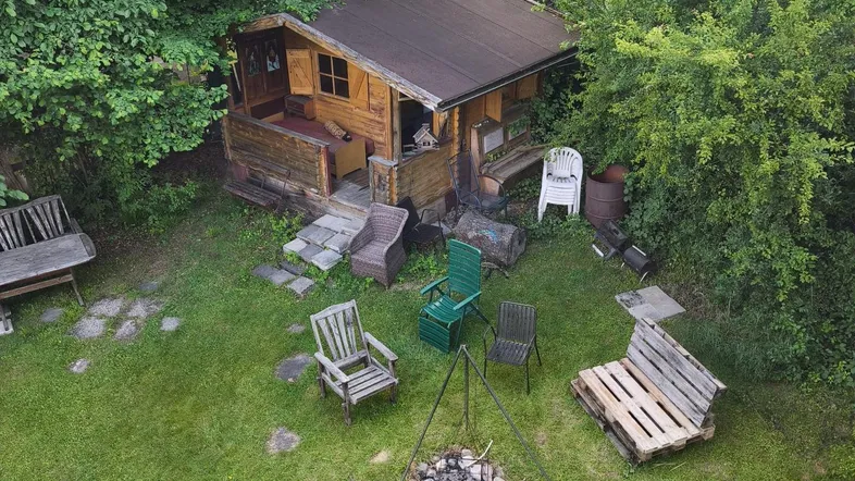 Rustikale Holzhütte in einem grünen Garten mit Feuerstelle und verschiedenen Sitzgelegenheiten.