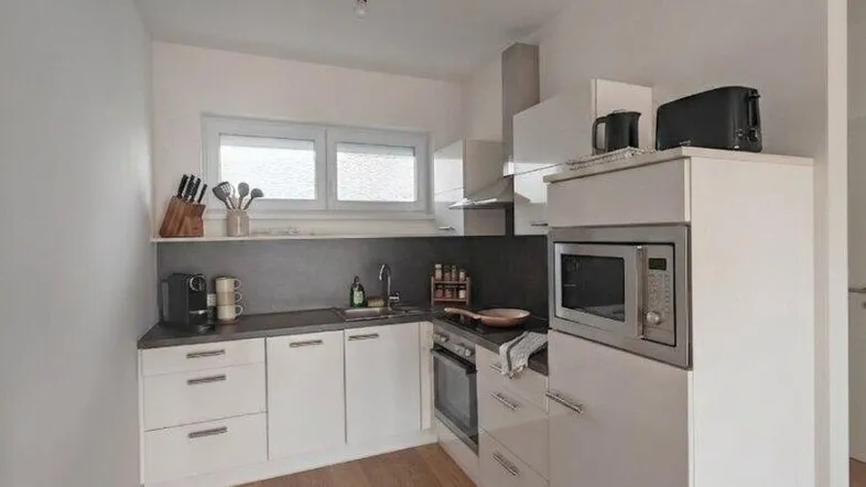Moderne Küche mit weißen Schränken, dunkler Arbeitsplatte, Holzboden und integrierten Geräten.