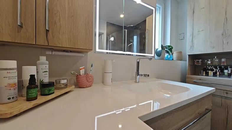 Detailansicht des modernen Waschbeckens mit Armatur und beleuchtetem Spiegelschrank.