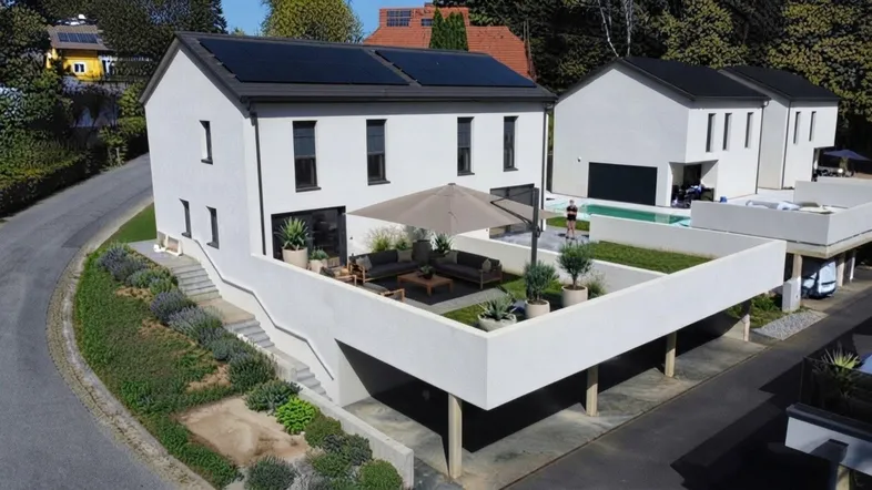 Modernes Einfamilienhaus mit Photovoltaikanlage, großer Terrasse und Carport, umgeben von Grün.