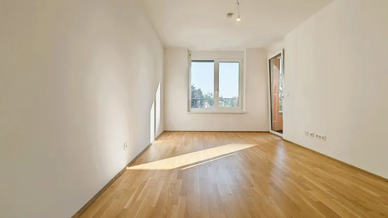 Helles Zimmer mit Parkettboden, weißen Wänden und Zugang zu einem Balkon.