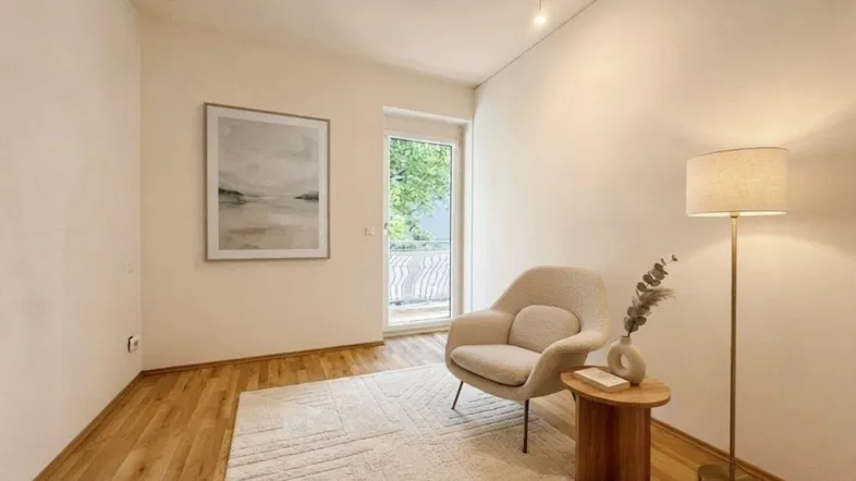 Helles Zimmer mit modernem Sessel, Holzboden und direktem Zugang zum Balkon.