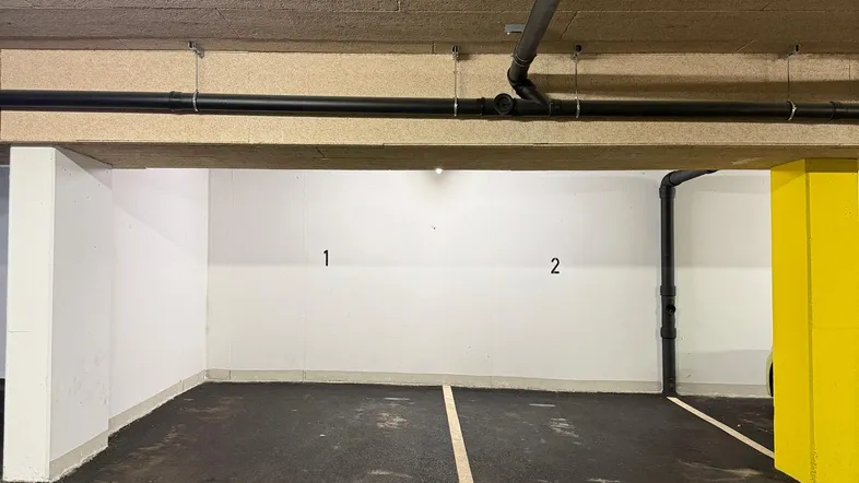 Leerer Stellplatz in einer Tiefgarage mit sichtbaren Leitungen an der Decke.