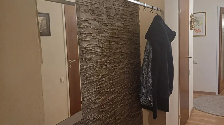 Heller Eingangsbereich mit dekorativer Steinwand, großem Spiegel und Garderobe auf Holzfußboden.