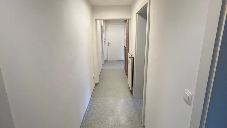 Heller Flur mit Einbaustrahlern und schlichten weißen Wänden, der zu weiteren Räumen führt.